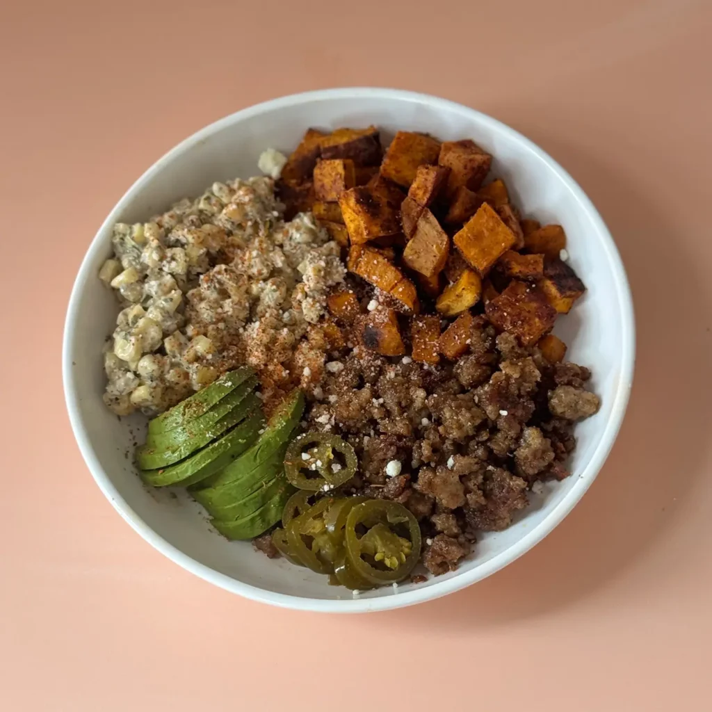 Street corn and sweet potato bowls with Jones sausage, topped with avocado, pickled jalapeños, and cotija cheese