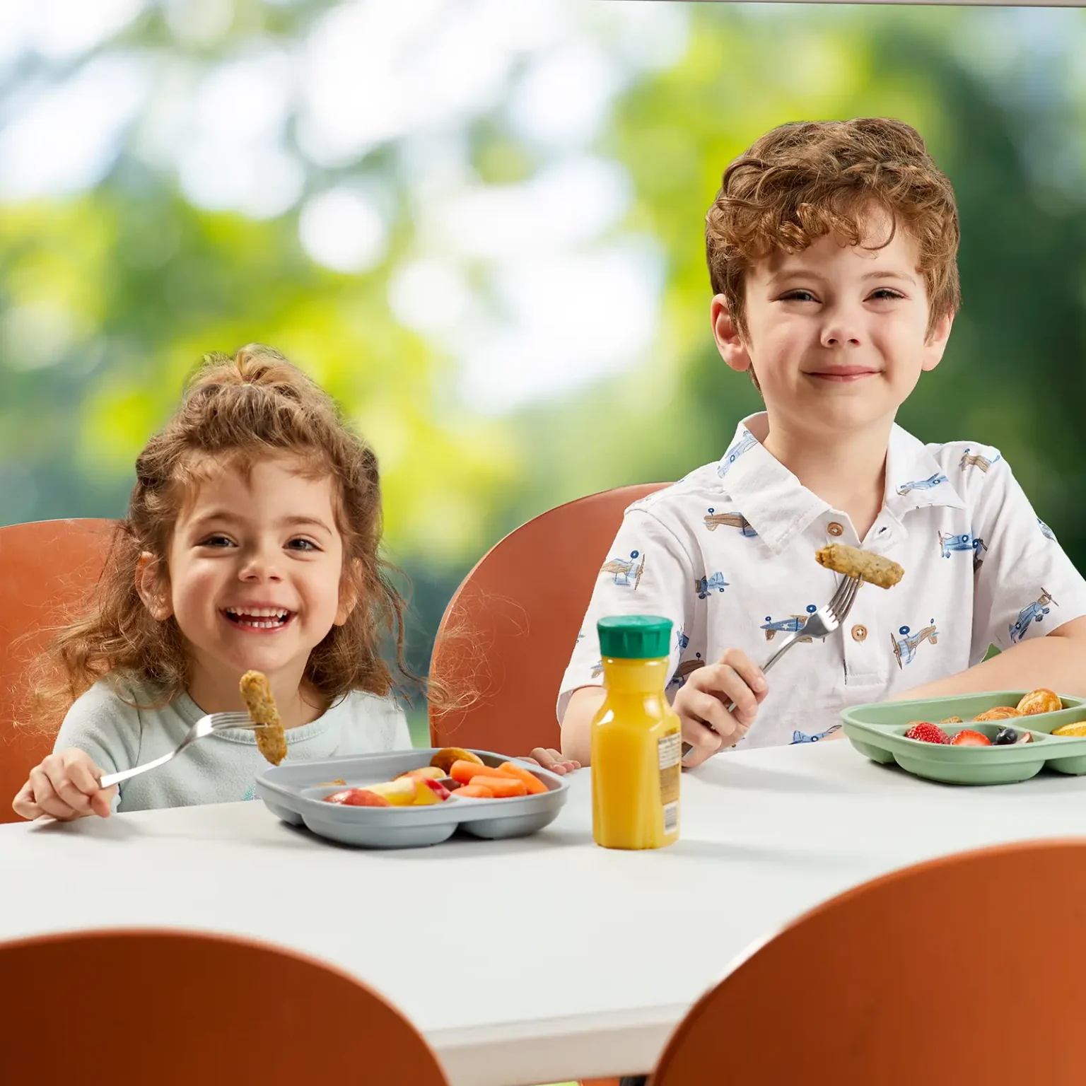 Two children smiling and eating Jones Dairy Farm chicken sausage at a school lunch table