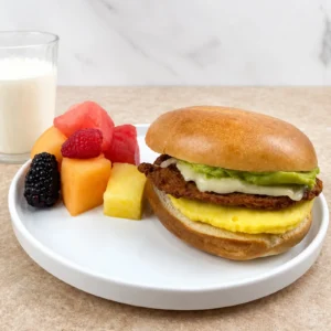 Jones Chicken Chorizo Sausage Brunch Bagel with egg patty, pepper jack cheese, and guacamole, served with fresh fruit and milk on a white plate