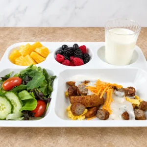 K-12 brunch bowl recipe: sliced Jones Pork Sausage Links over scrambled eggs with country gravy and shredded cheddar, plated on a school lunch tray with salad, fruit, and milk
