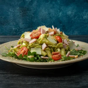 plate of spring pesto pasta with Canadian bacon, topped with halved cherry tomatoes, shaved Pecorino Romano, diced Jones Dairy Farm Canadian Bacon, and toasted breadcrumbs, served over a bed of fresh baby arugula.