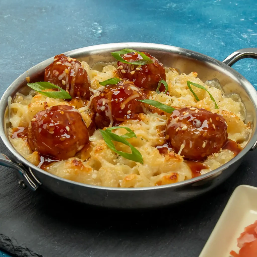 Skillet of baked cavatappi mac and cheese topped with glazed Jones Pork and Bacon Meatballs, sesame seeds, and scallions