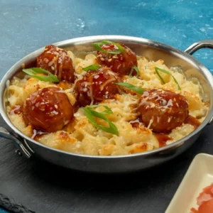 Skillet of baked cavatappi mac and cheese topped with glazed Jones Pork and Bacon Meatballs, sesame seeds, and scallions