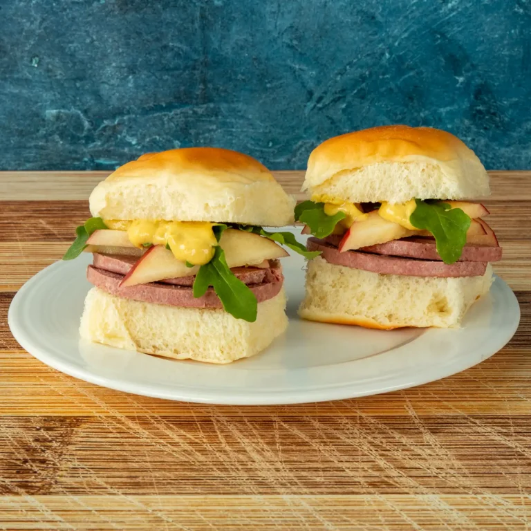 Two Braunschweiger, apple, and arugula sliders on Hawaiian rolls, cut in half on a plate.