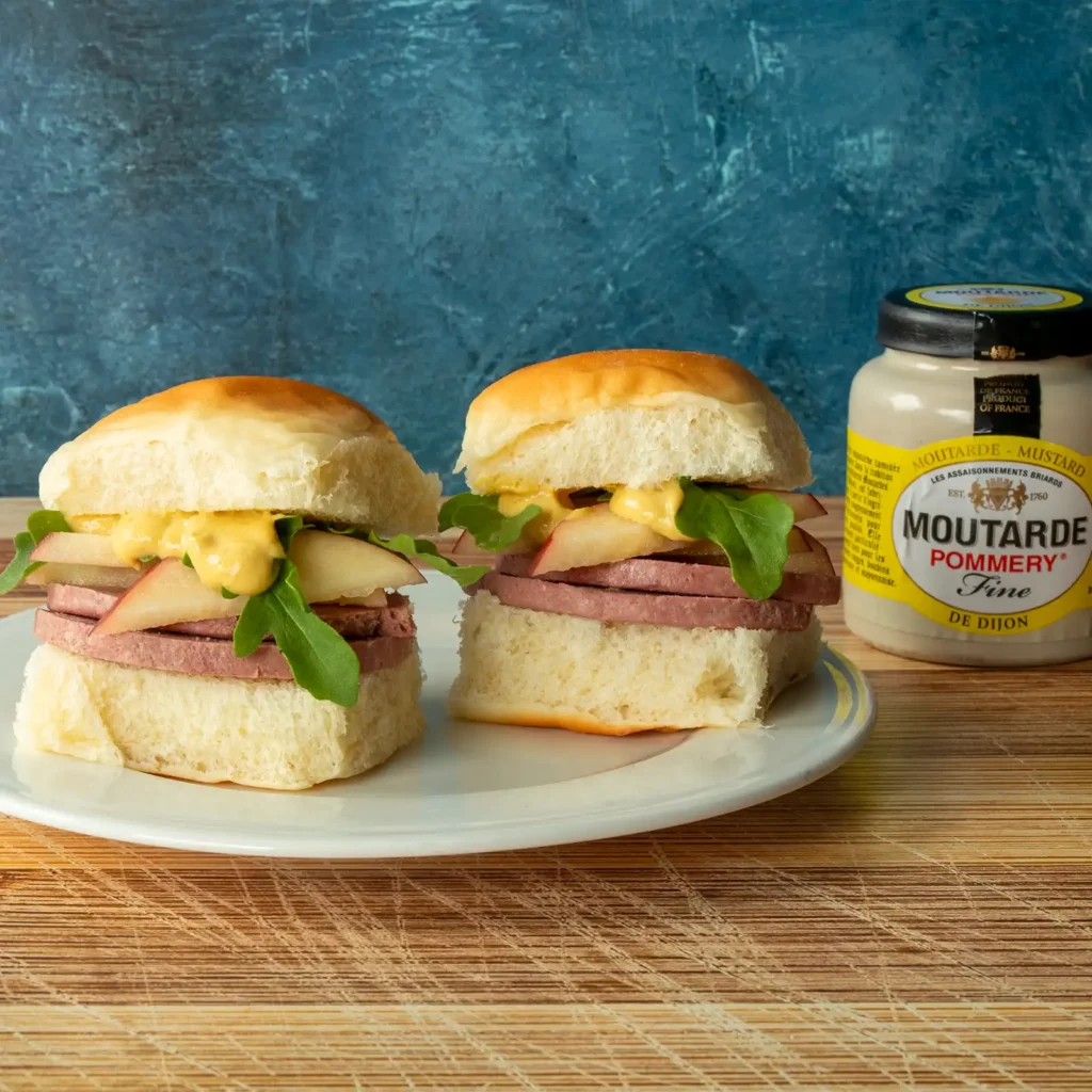 Braunschweiger, apple, and arugula sliders on a plate next to a jar of Moutarde Pommery Dijon.
