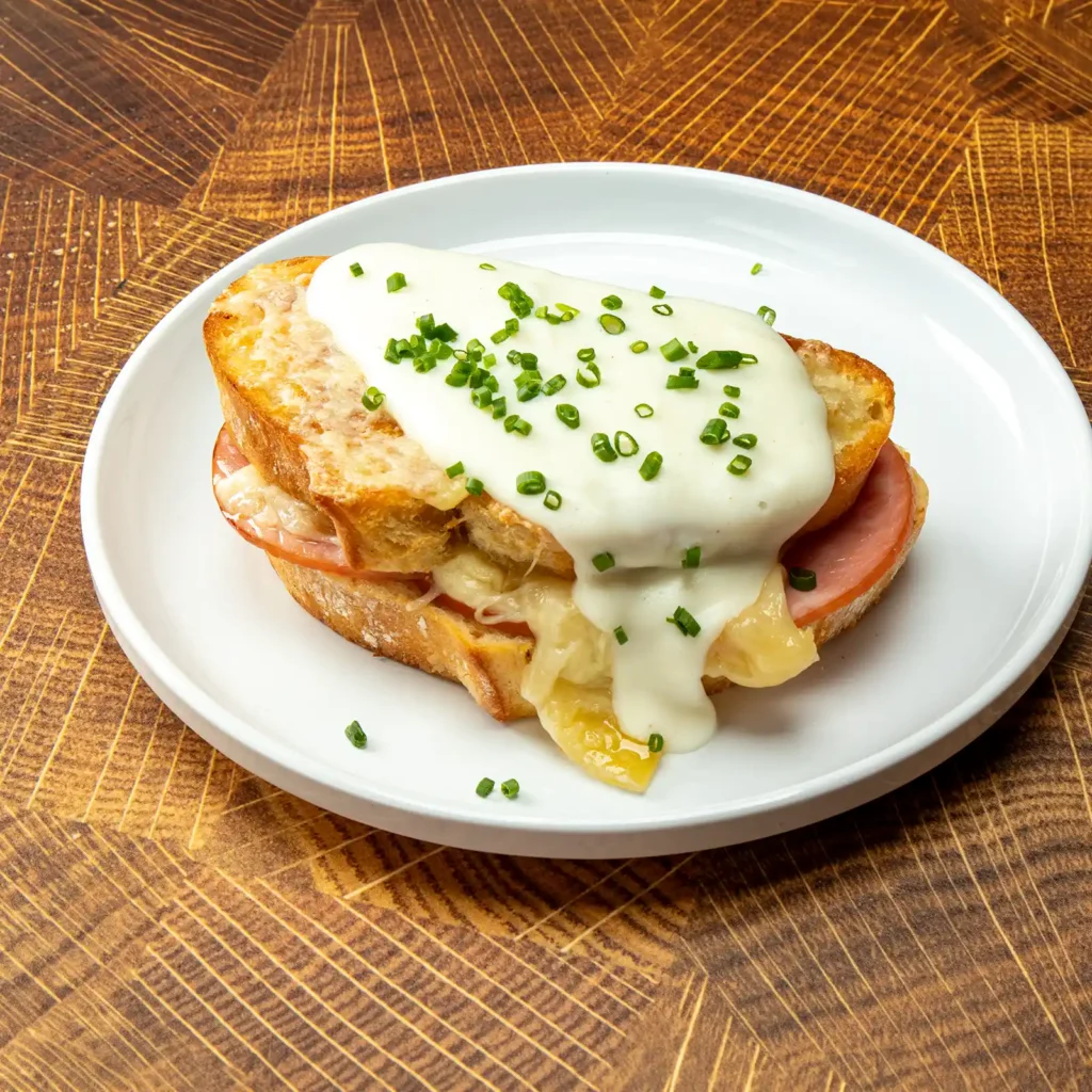 Croque monsieur with Jones Canadian Bacon, gruyere cheese, and béchamel sauce on griddled French bread, topped with fresh chives