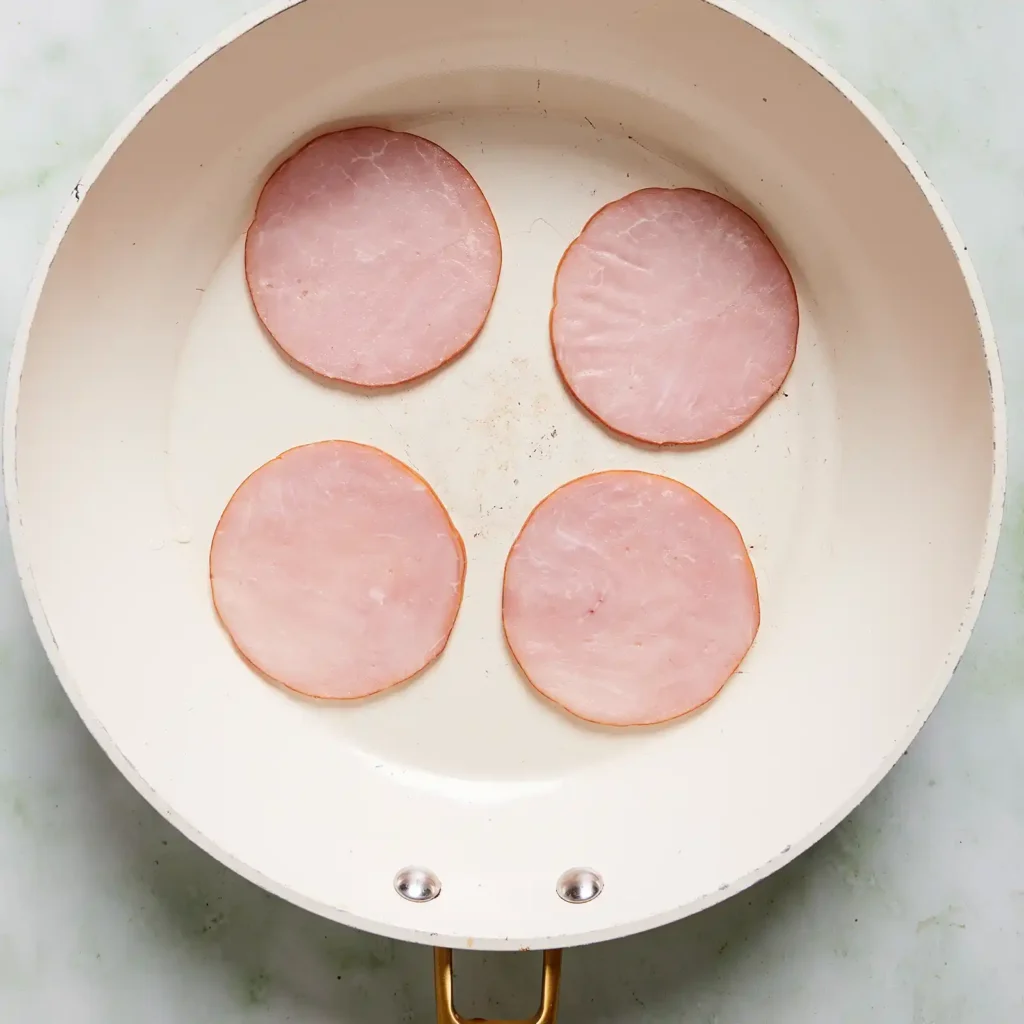 Four slices of Jones Canadian bacon cooking in a skillet, part of the prep for a high protein snack box.