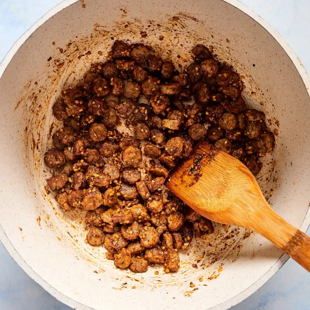 Sliced Jones chicken sausage browning in a pot with garlic and spices, the first step in making white chicken sausage chili.