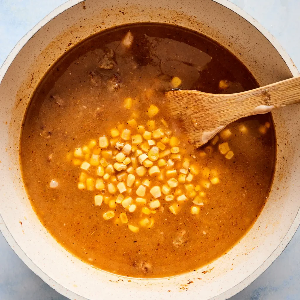 Chicken broth, salsa verde, and corn simmering together in a pot for creamy white chicken sausage chili.