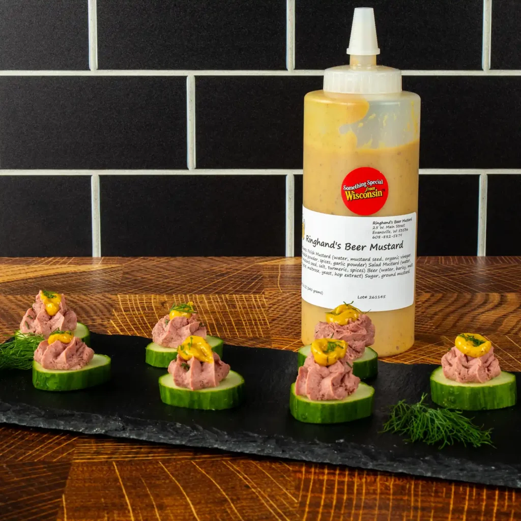 Cucumber bites with whipped Braunschweiger and mustard, served on a slate board next to a bottle of Ringhand's Beer Mustard.
