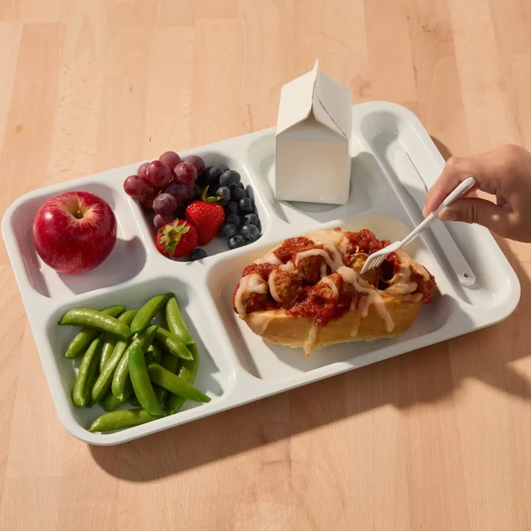 School lunch tray with a meatball sub topped with marinara and melted cheese, sugar snap peas, an apple, mixed berries, and a milk carton.