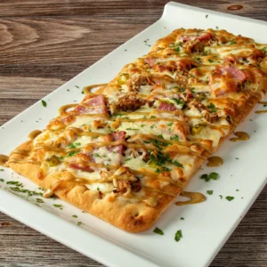 Cubano flatbread with mornay sauce, roast pulled pork, Jones Breakfast Ham, dill pickles, and mozzarella, finished with honey mustard drizzle and parsley