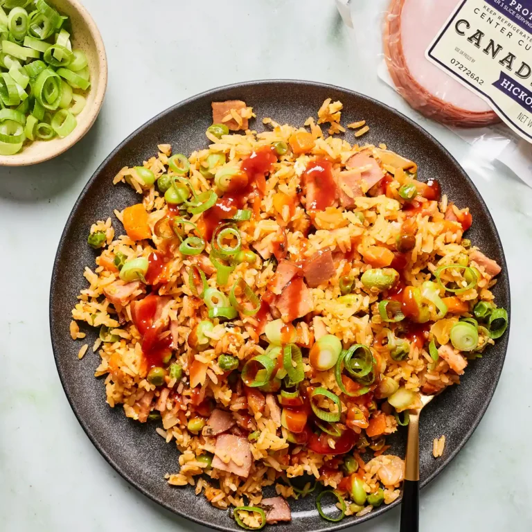 Overhead view of a plate of kimchi fried rice with Canadian bacon, topped with green onion and sriracha, next to a bowl of sliced green onion and a package of Jones Canadian bacon.