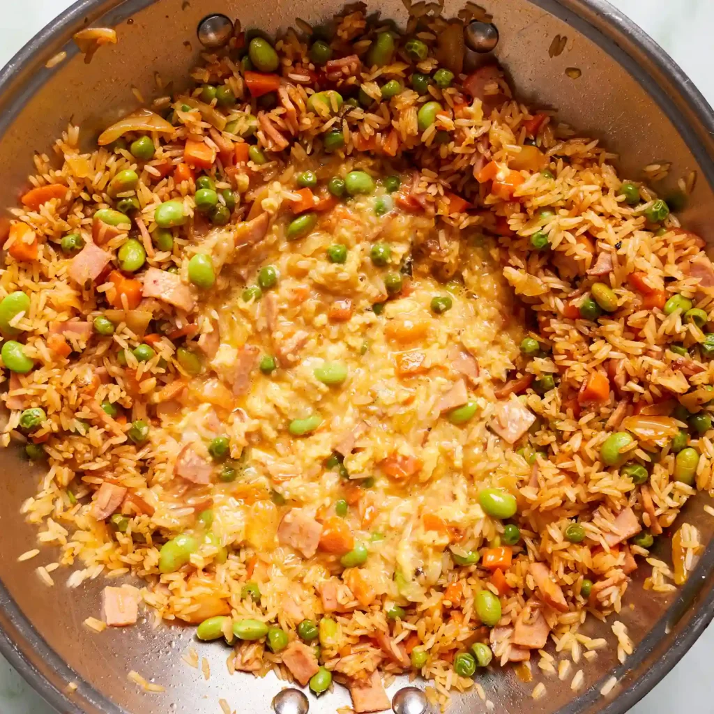 Kimchi fried rice with Canadian bacon, vegetables, and scrambled egg being combined in a wok.