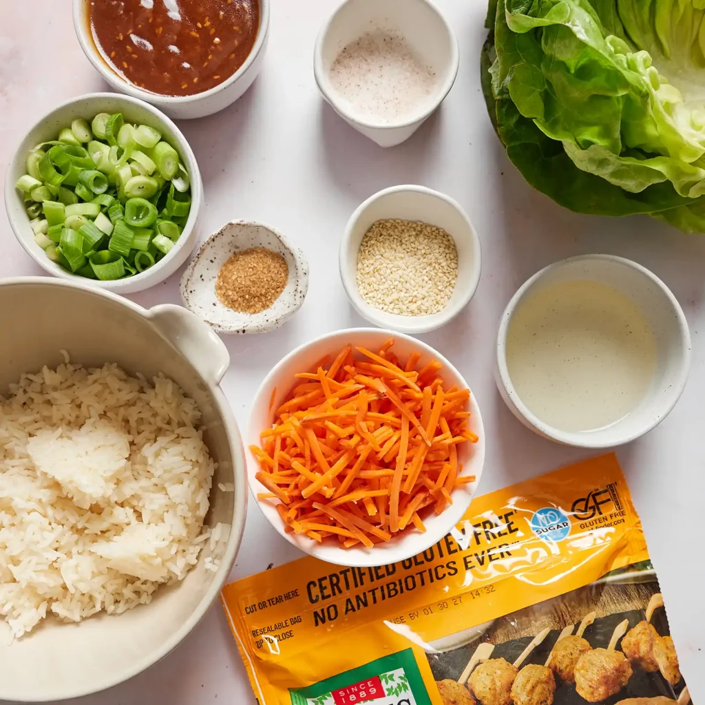 Ingredients for lettuce wraps with soy sesame meatballs, including a package of Jones Dairy Farm chicken meatballs, soy sesame sauce, shredded carrots, rice, butter lettuce, sesame seeds, green onion, and salt.
