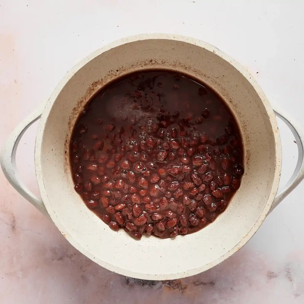 Black beans simmering in a pot, prepared as a topping for a taco rice bowl.