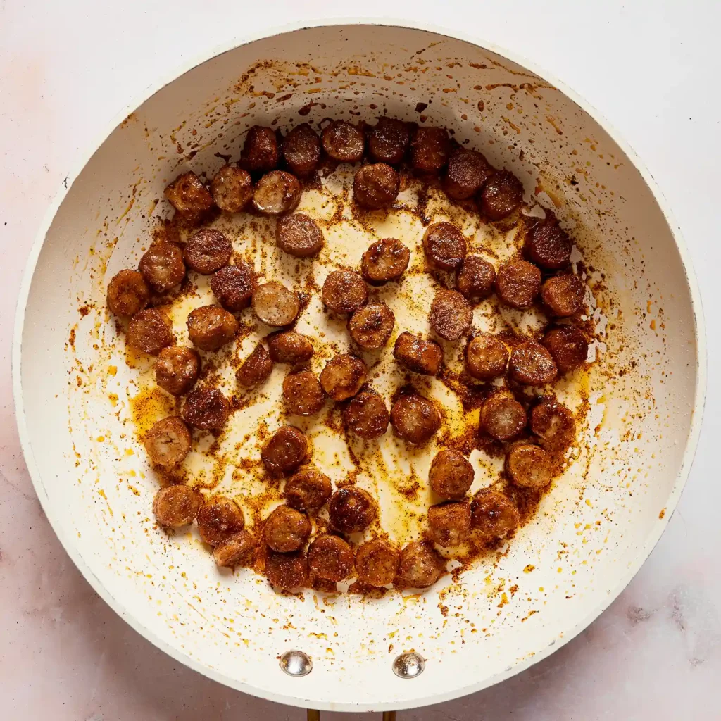 Sliced Jones sausage cooking in a skillet with taco seasoning, prepared for a taco rice bowl.