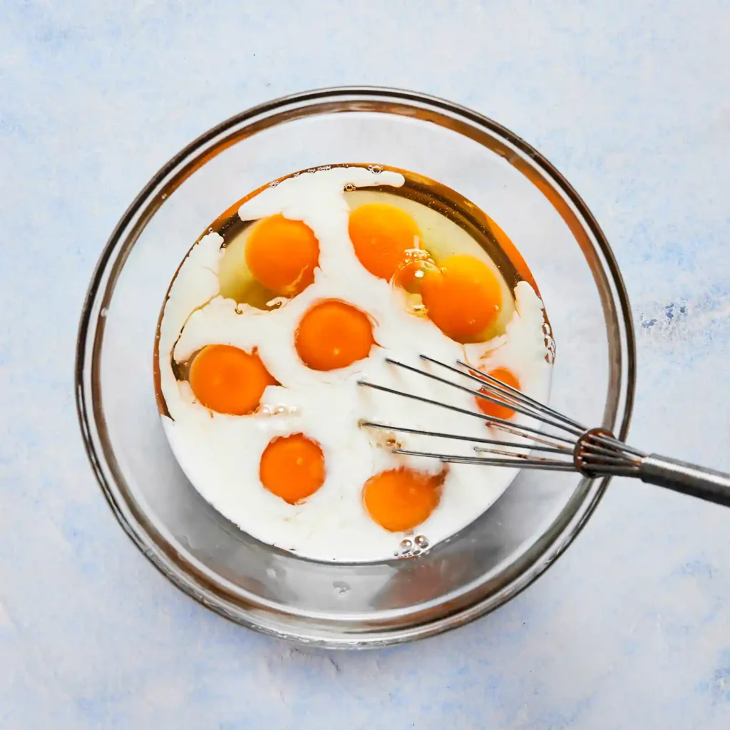 Whisked eggs and milk in a glass bowl with a metal whisk, ready to bake for meal prep breakfast bowls.
