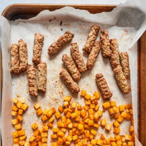 Roasted chicken sausage links and diced seasoned potatoes on a parchment-lined baking sheet.