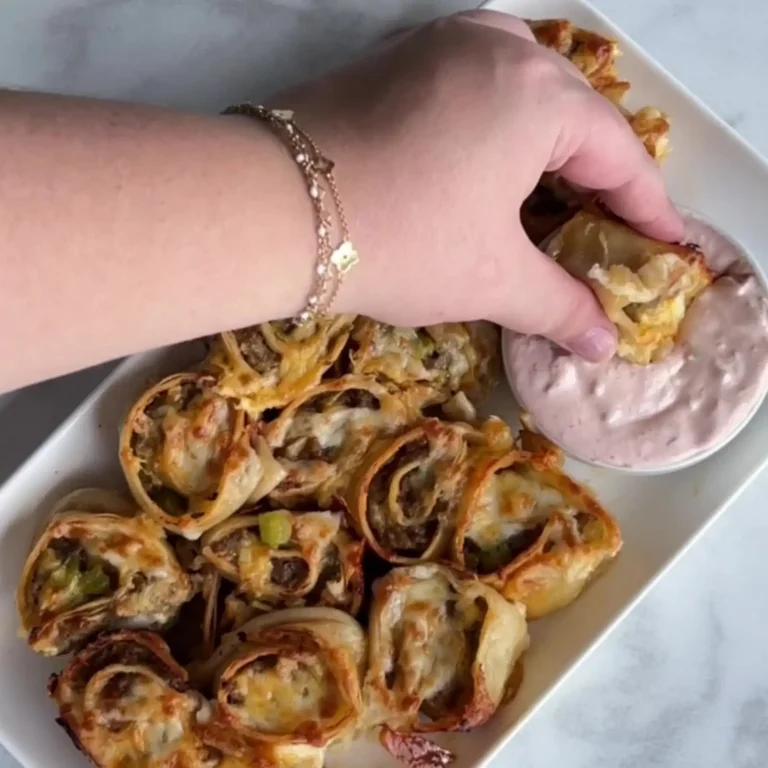 Hand dipping a baked Mexican sausage pinwheel into creamy salsa dip, with a platter of pinwheels alongside