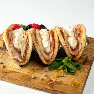 Pumpkin Spice Pancake Tacos with Jones Heritage Uncured Ham and cinnamon whipped cream cheese, garnished with cinnamon chips and hot honey, served upright in a taco holder with fresh berries and mint