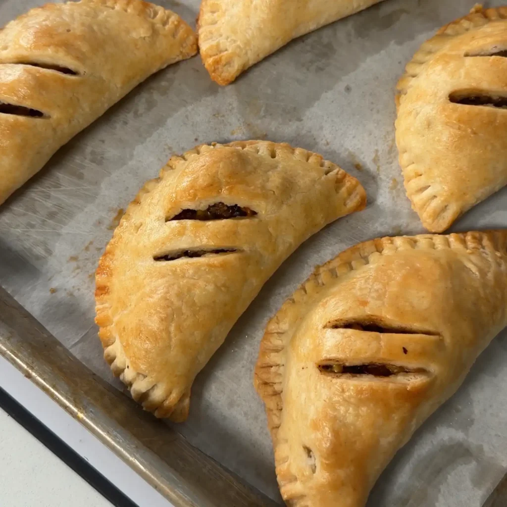 Golden-baked hand pies with crimped edges and vented slits, cooling on a parchment-lined baking sheet.