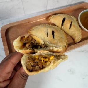 Hand pie split open, revealing sausage and melted cheddar filling, served on a wood tray with a side of mango hot honey dipping sauce.