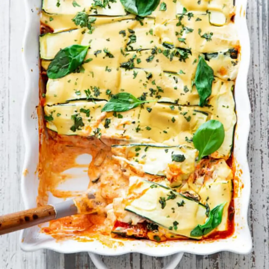 A slice of zucchini lasagna being lifted from the baking dish with a spatula, showing the layered zucchini, sauce, and cashew cheese sauce.
