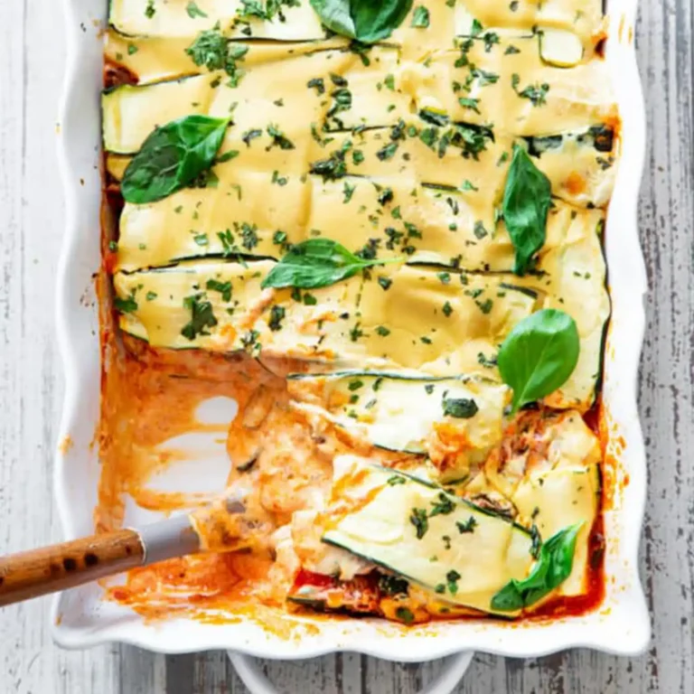 A slice of zucchini lasagna being lifted from the baking dish with a spatula, showing the layered zucchini, sauce, and cashew cheese sauce.