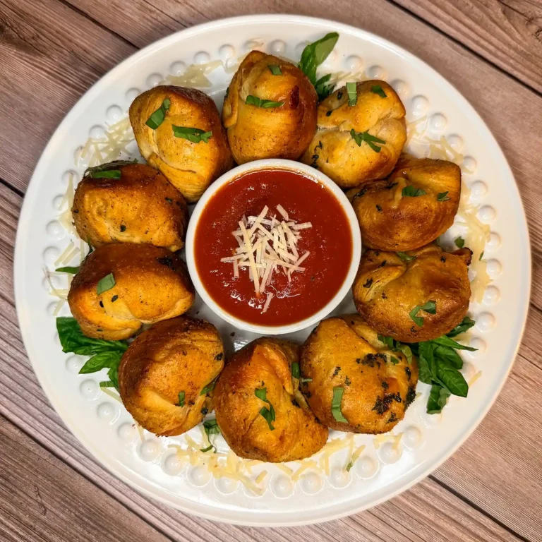 Cheesy meatball bombs arranged in a ring around a bowl of marinara sauce, garnished with basil and parmesan
