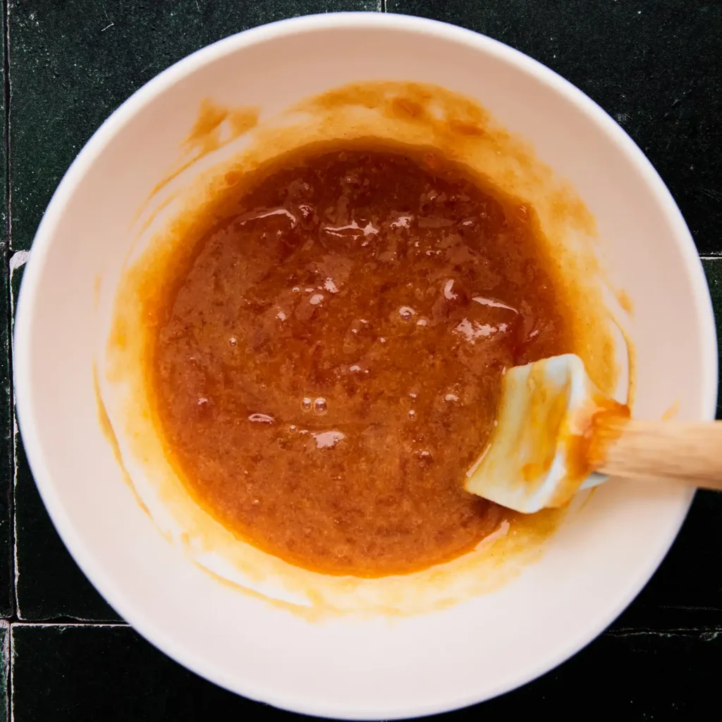 Apricot Dijon glaze in a bowl, being brushed with a pastry brush.