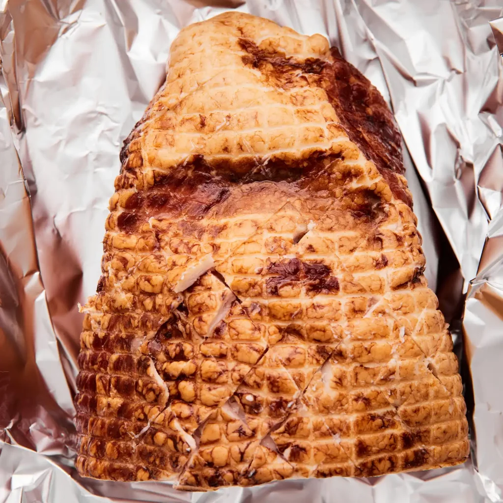 Close-up of a scored, glazed ham resting in foil after roasting.