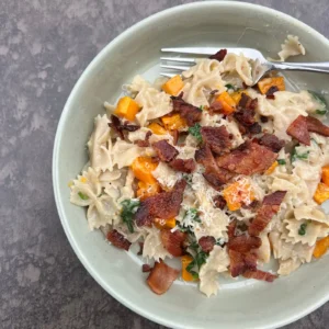 Farfalle pasta with roasted butternut squash, bacon, spinach, and parmesan in a bowl.