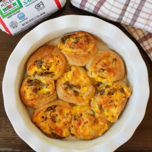 Savory breakfast rolls baked in a dish with a package of Jones sausage and a checkered towel.