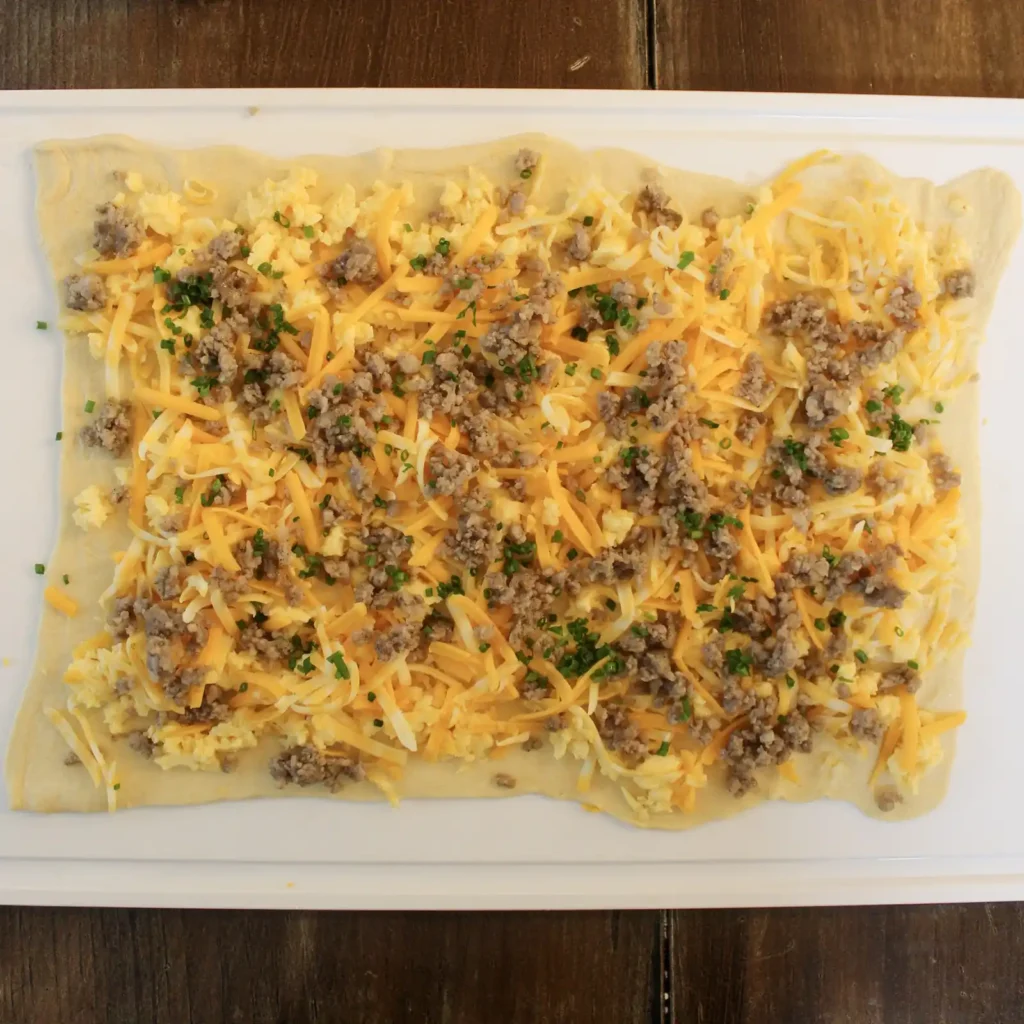 Crescent dough topped with sausage, scrambled egg, shredded cheese, and chives before rolling.