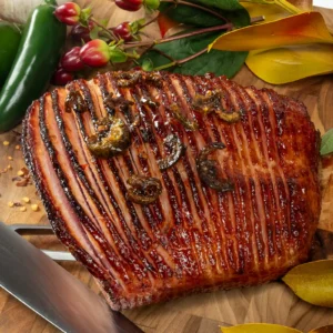 Hasselback ham glazed with sweet pineapple chili crisp, garnished with dried chilies, on a wood board with jalapeño