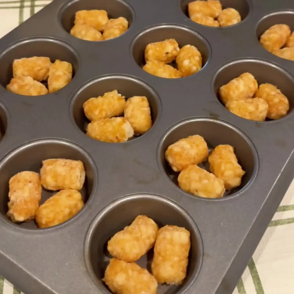 Raw tater tots arranged in a muffin tin before baking, three per cup.