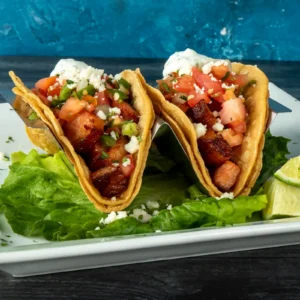 Crispy hard-shell tacos filled with seared bacon slab pieces, pico de gallo, queso fresco, and cilantro lime crema, served on a bed of lettuce