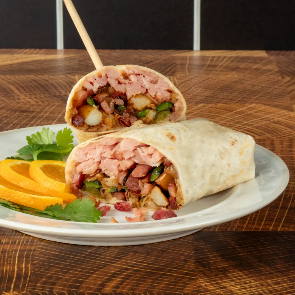Pulled bacon breakfast burrito halves on a plate with orange slices and cilantro, showing potato, pepper, shredded pulled bacon, and diced bacon