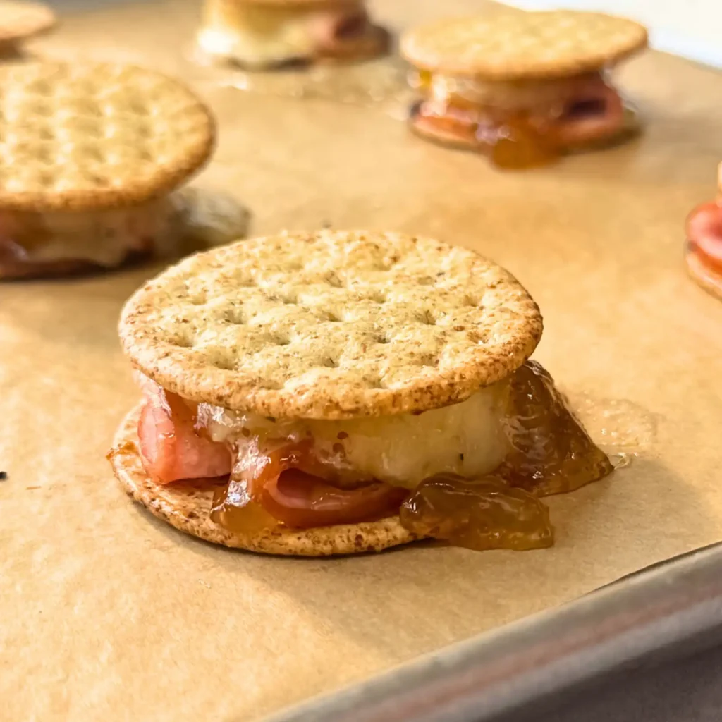 Broiled cracker sandwich with melted cheese and fig jam oozing between the layers of Canadian bacon.