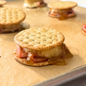 Broiled cracker sandwich with melted cheese and fig jam oozing between the layers of Canadian bacon.