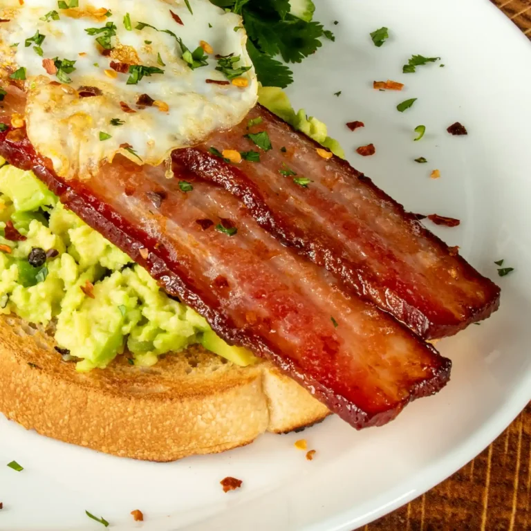 Close-up of thick-cut seared bacon slices, fried egg, and smashed avocado on toasted sourdough