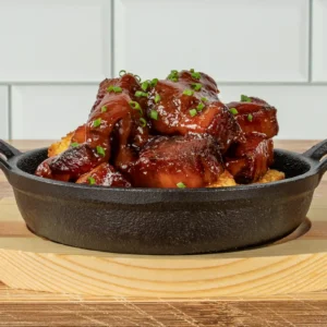 Bacon slab burnt ends glazed in barbecue sauce over cornbread in a cast iron skillet, topped with chives