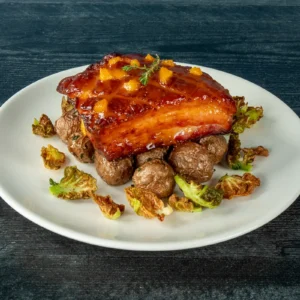 Seared bacon slab over roasted potatoes and crispy fried Brussels sprout leaves on a white plate