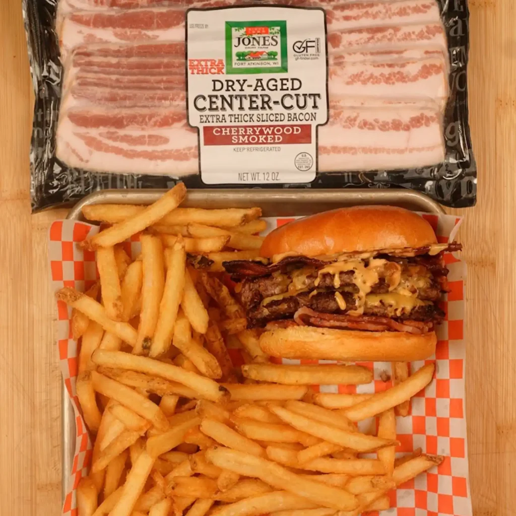 Double-patty bacon burger with fries on a tray, shown below a package of Jones Dry Aged Center Cut Extra Thick Cherrywood Smoked Bacon